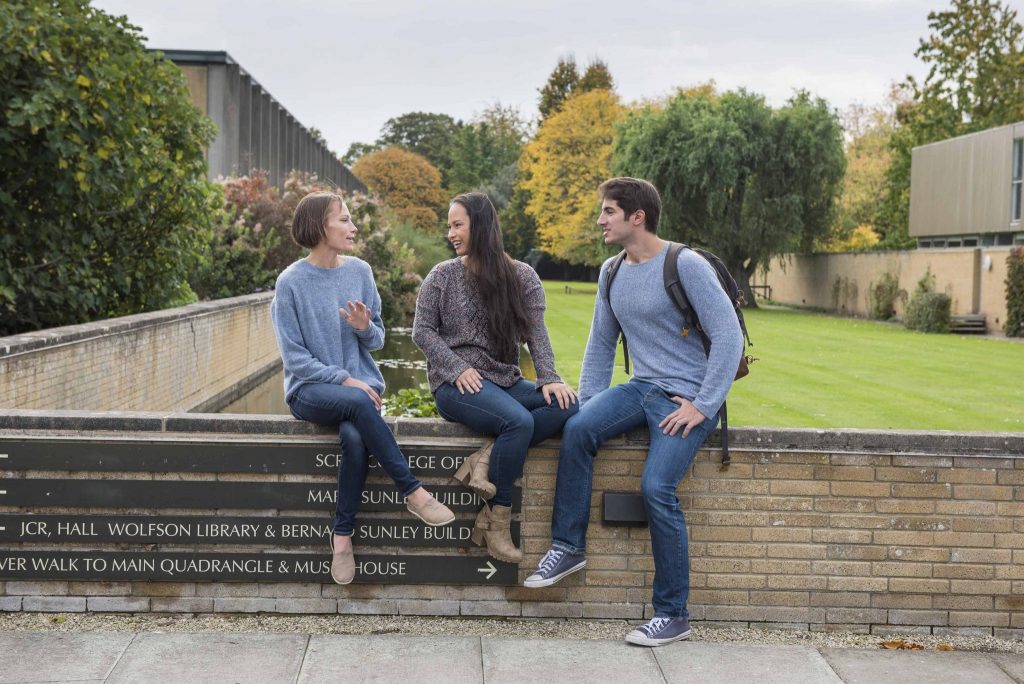 University students talking on a wall with trees in the background