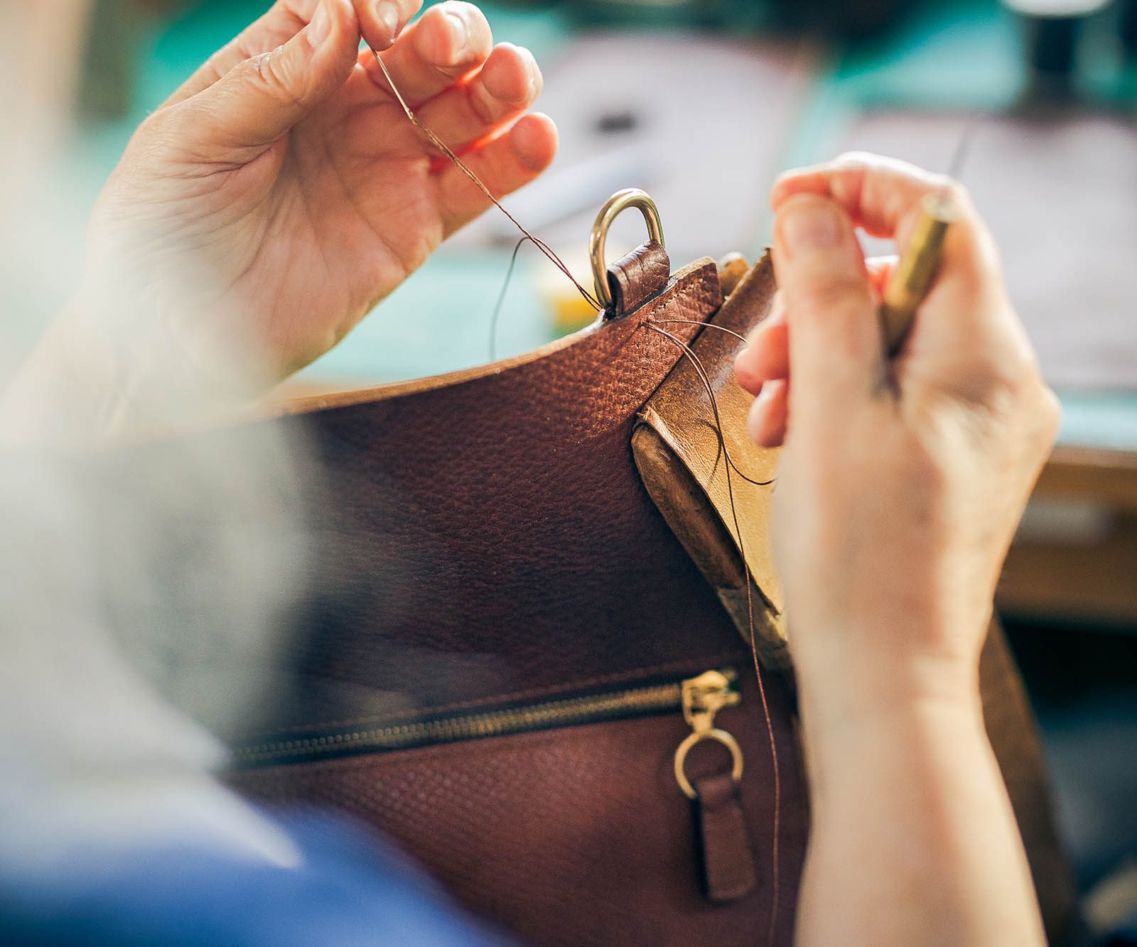 a woman's hands stitching leather