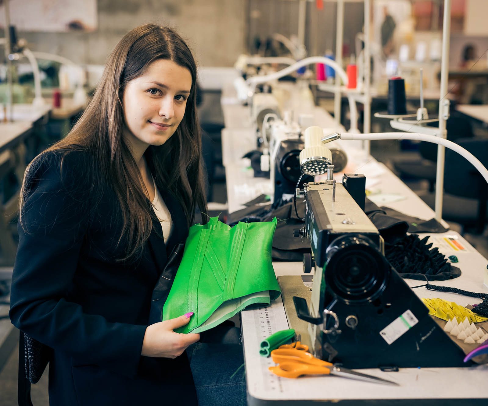 woman in black suit at a sewing machine holding green leather
