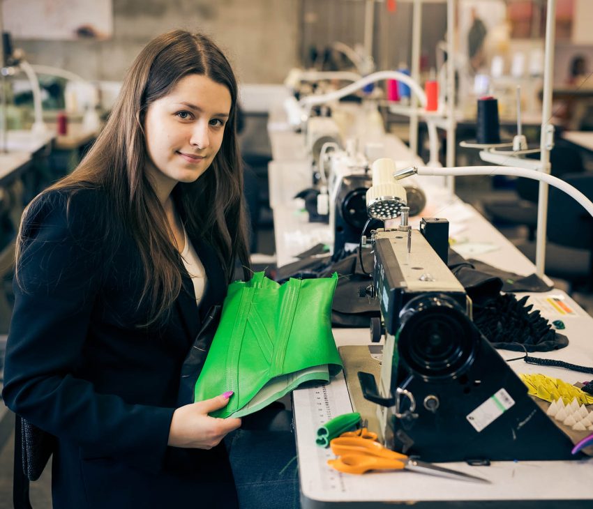 woman in black suit at a sewing machine holding green leather
