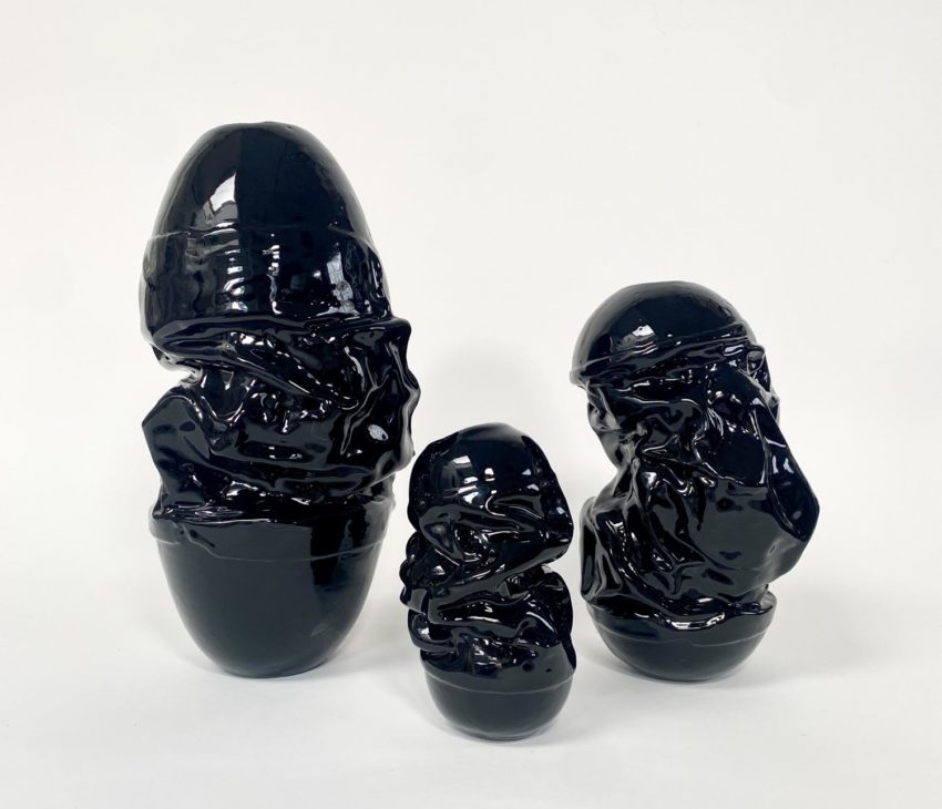 Three glossy, black, irregularly shaped ceramic sculptures of varying heights are arranged side by side against a plain white background.